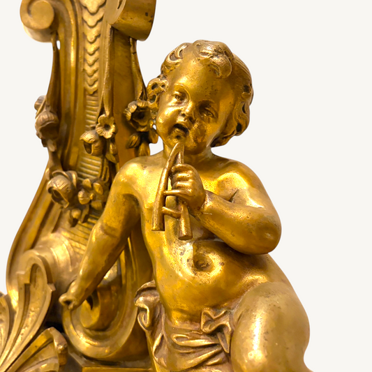 KLS Vaults Louis XVI style gilt-bronze andiron featuring a finely chased putto playing a flute with acanthus details