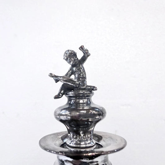 KLS Vaults antique 1902 sterling silver stopper featuring a seated putto finial on an Edwardian glass decanter