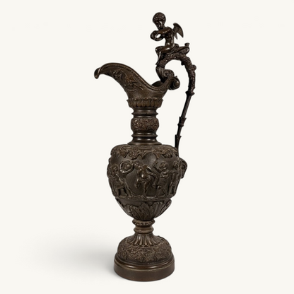 KLS Vaults 19th-century neoclassical bronze ewer with high-relief putti frieze, winged cherub finial, and brown patina.