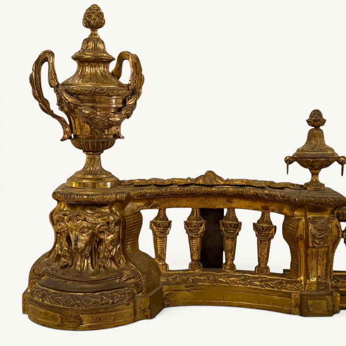 KLS Vaults Louis XVI style gilt-bronze fire fender with ram's head masks, neoclassical urns, and pierced balustrade.