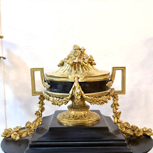 Decorative gold urn on a black pedestal against a white background