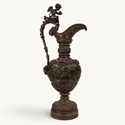 KLS Vaults 19th-century neoclassical bronze ewer with high-relief putti frieze, winged cherub finial, and brown patina.