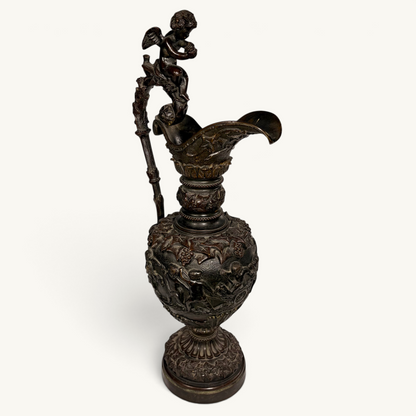 KLS Vaults 19th-century neoclassical bronze ewer with high-relief putti frieze, winged cherub finial, and brown patina.