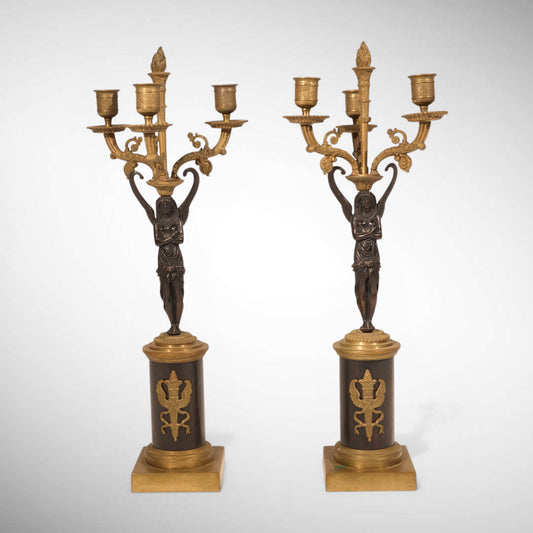 A PAIR OF EGYPTIAN REVIVAL PATINATED AND GILT BRONZE FIGURAL THREE-LIGHT CANDELABRA