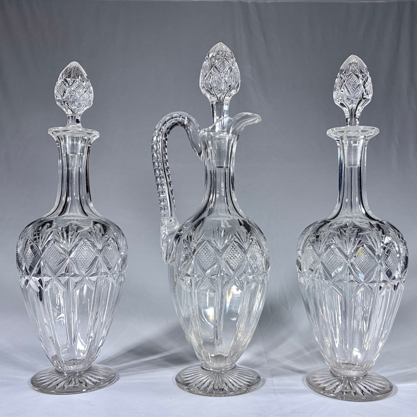 KLS Vaults 19th-century cut-glass set with two decanters and a claret jug featuring diamond-cut patterns and stoppers.