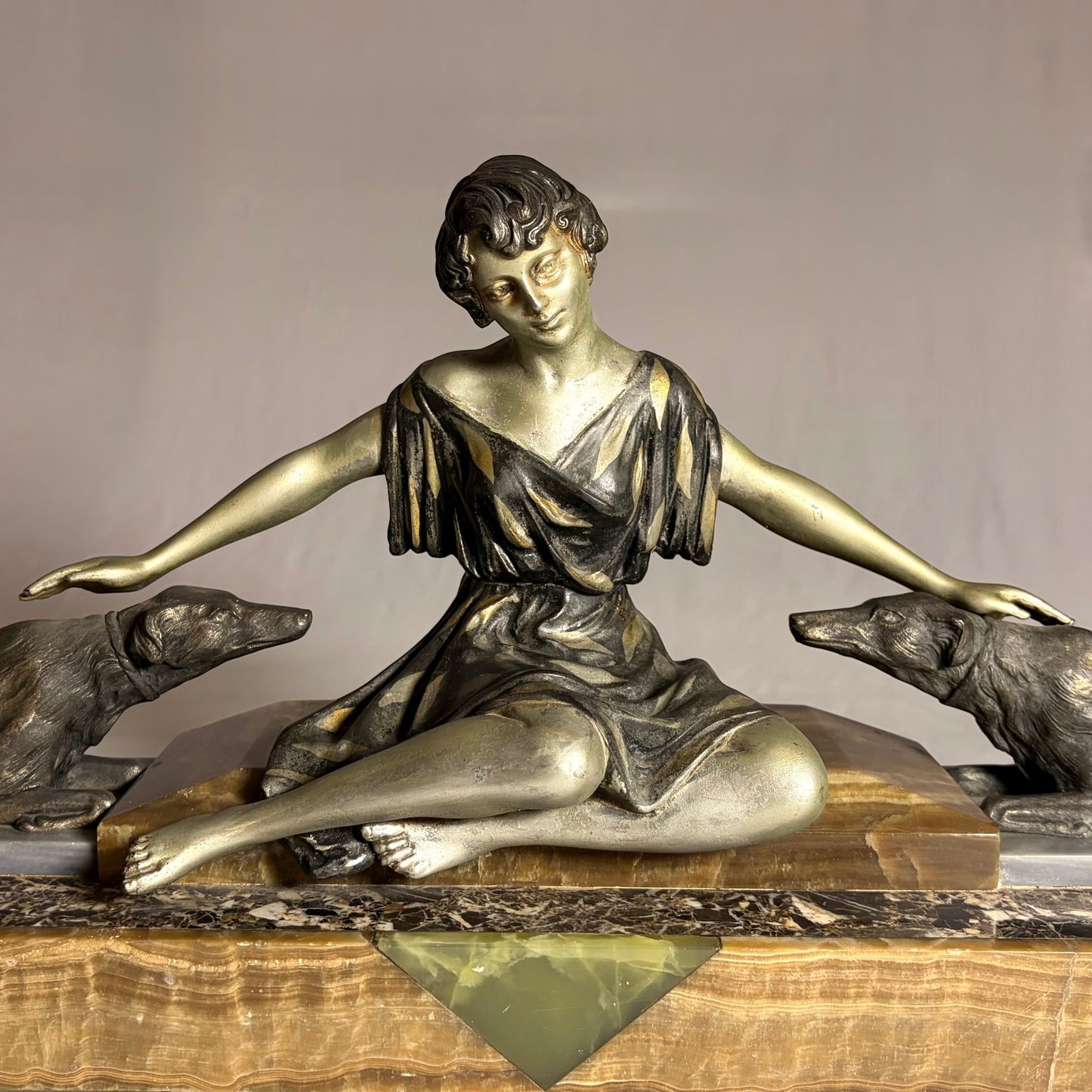 KLS Vaults Art Deco spelter figural group of a seated woman with two hounds on an onyx and marble plinth, circa 1920s.