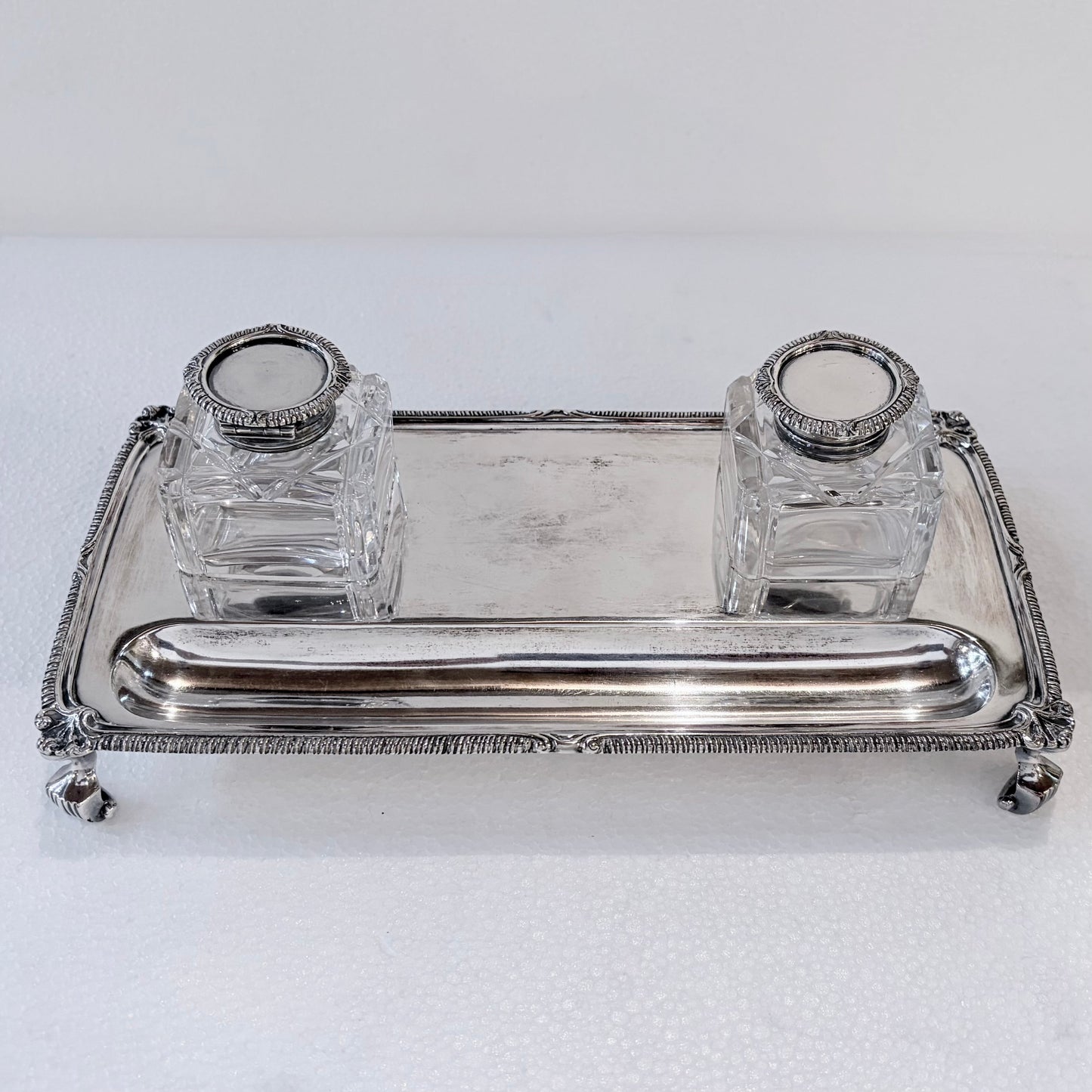 KLS Vaults Edwardian sterling silver inkstand with gadrooned border, claw-and-ball feet, and two square glass inkwells.