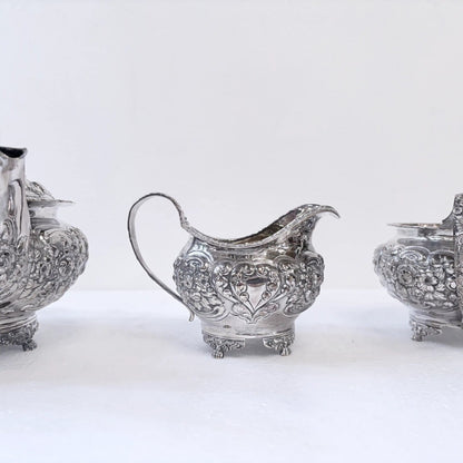 KLS Vaults 1822 sterling silver tea service featuring ornate repoussé floral chasing and shell-motif bracket feet.