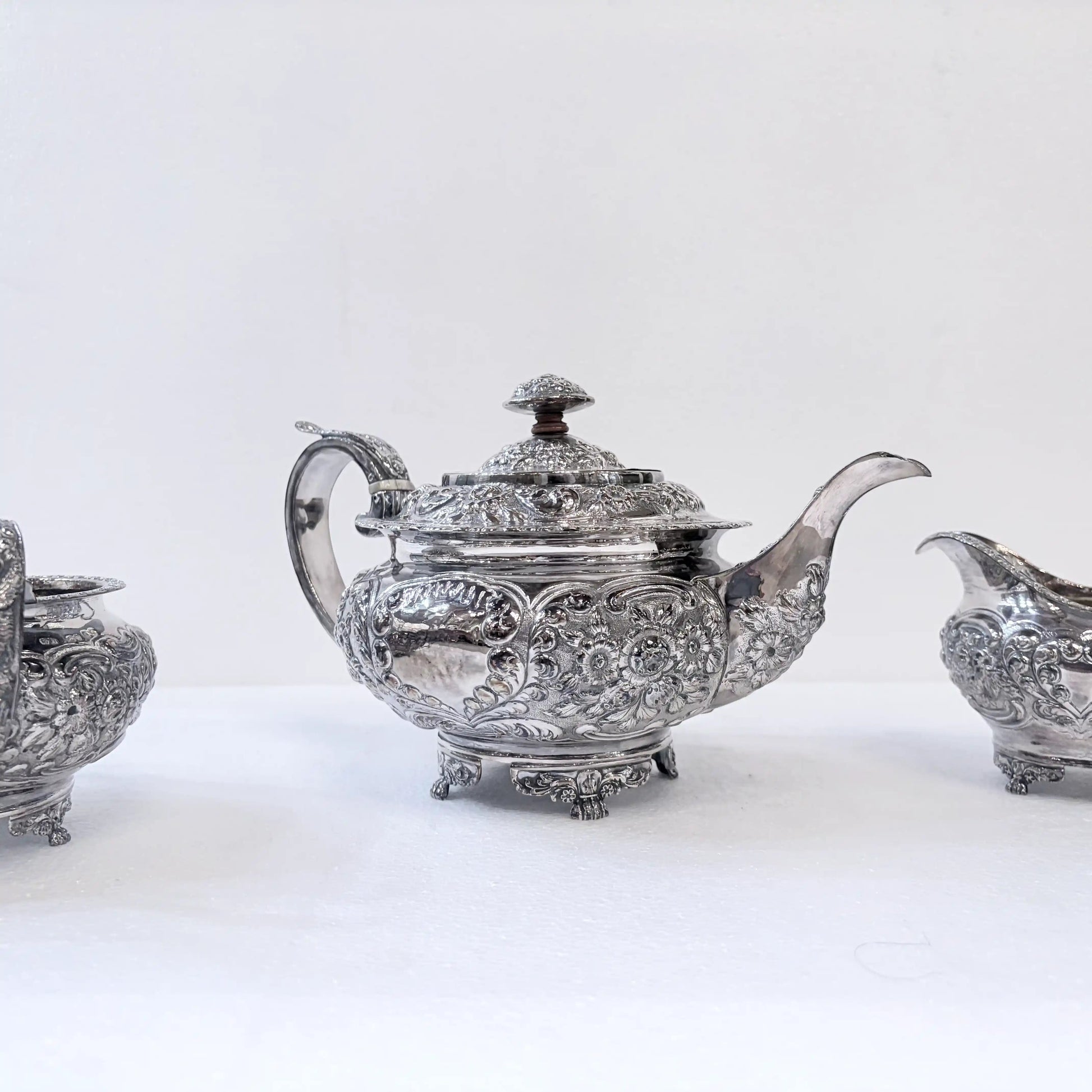 KLS Vaults 1822 sterling silver tea service featuring ornate repoussé floral chasing and shell-motif bracket feet.