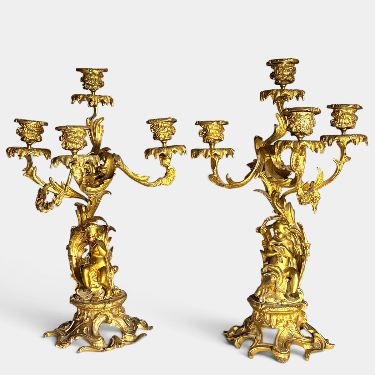 KLS Vaults pair of 19th-century Louis XV style gilt bronze four-light candelabra featuring putti and acanthus foliage.