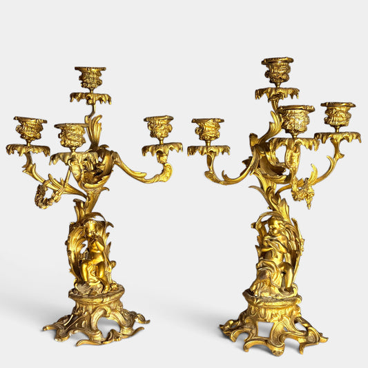 KLS Vaults pair of 19th-century Louis XV style gilt bronze four-light candelabra featuring putti and acanthus foliage.