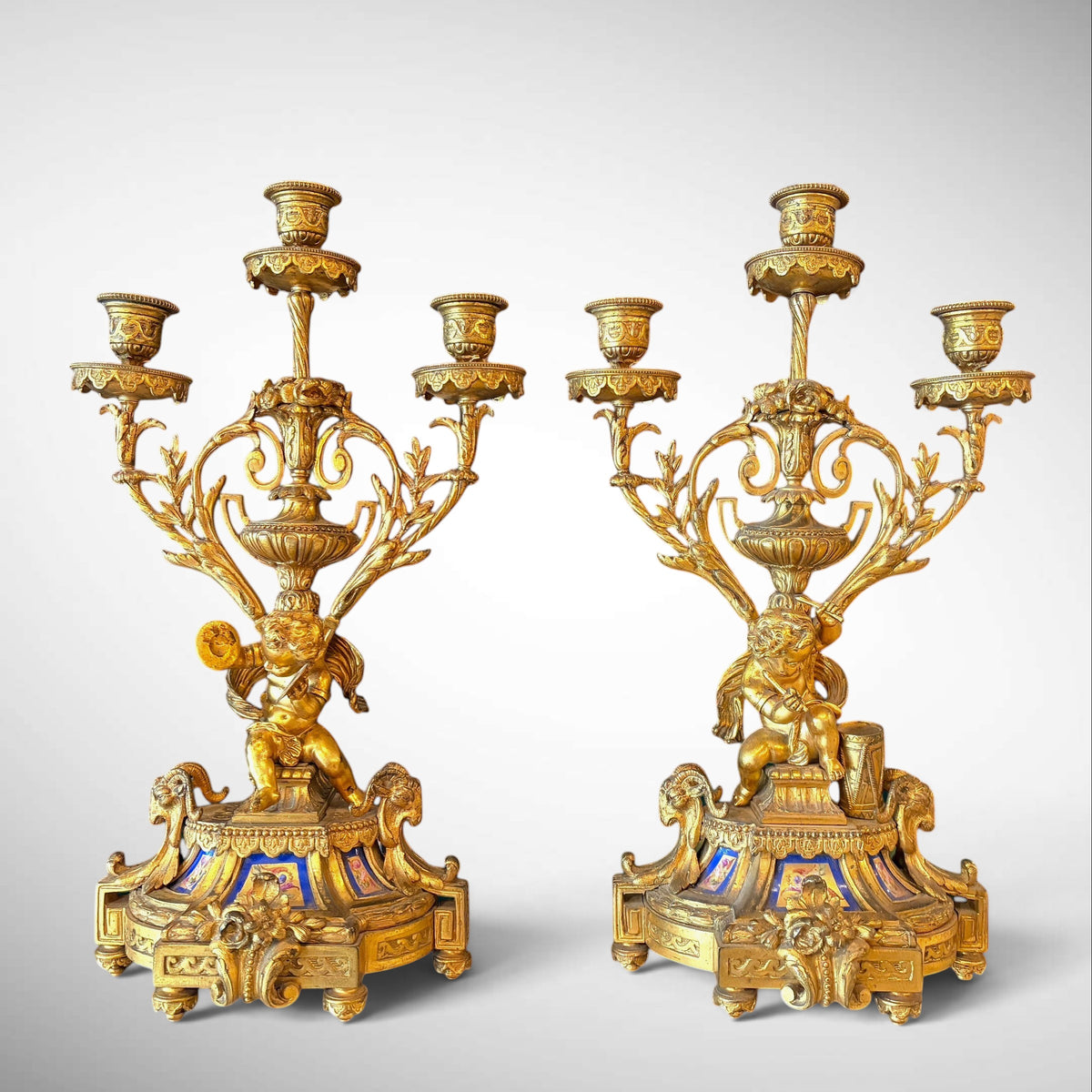 KLS Vaults pair of 19th-century gilt-bronze candelabra with putti figures and blue Sevres-style porcelain plaques.