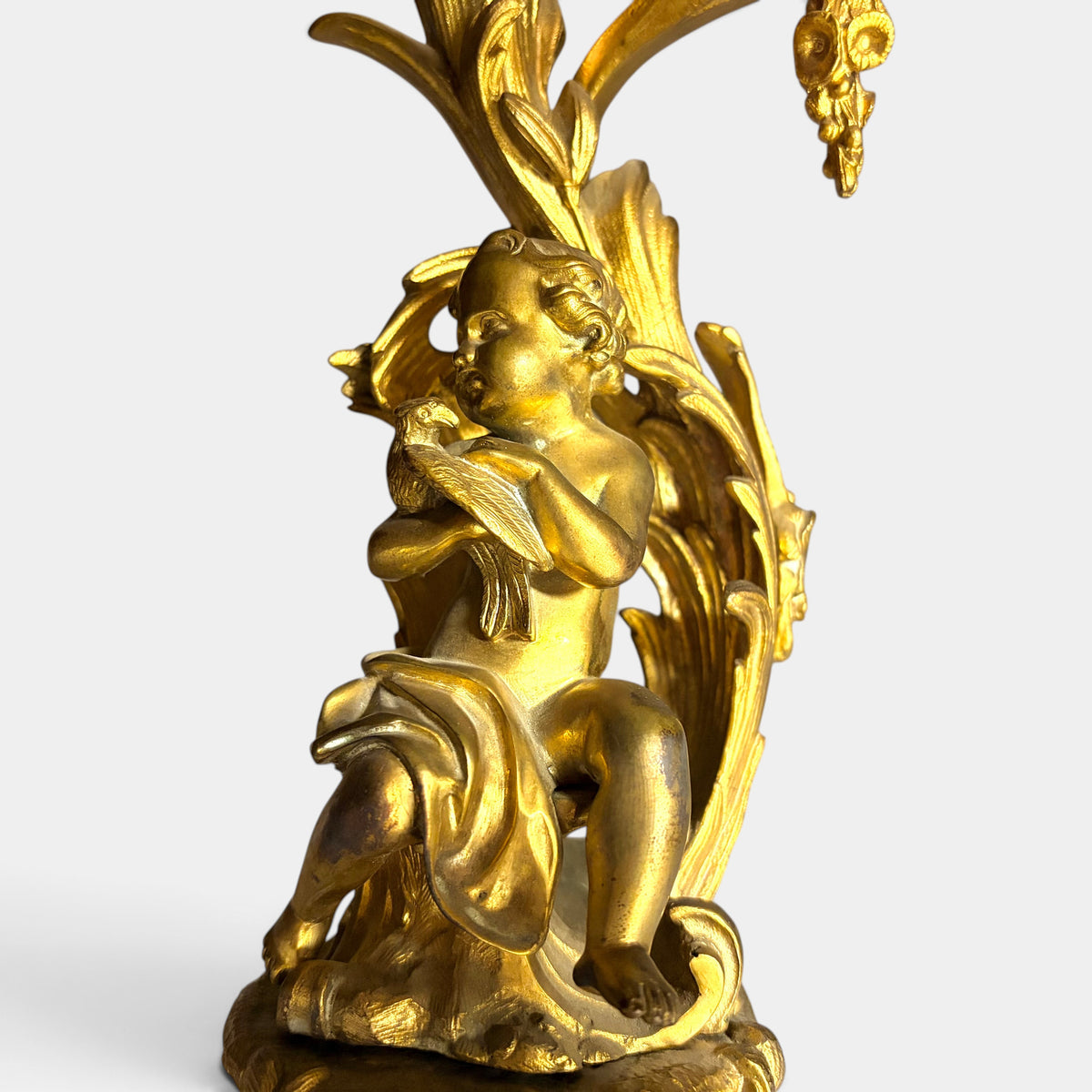 KLS Vaults 19th century Louis XV style gilt bronze candelabrum featuring a seated putto figure and acanthus foliage.