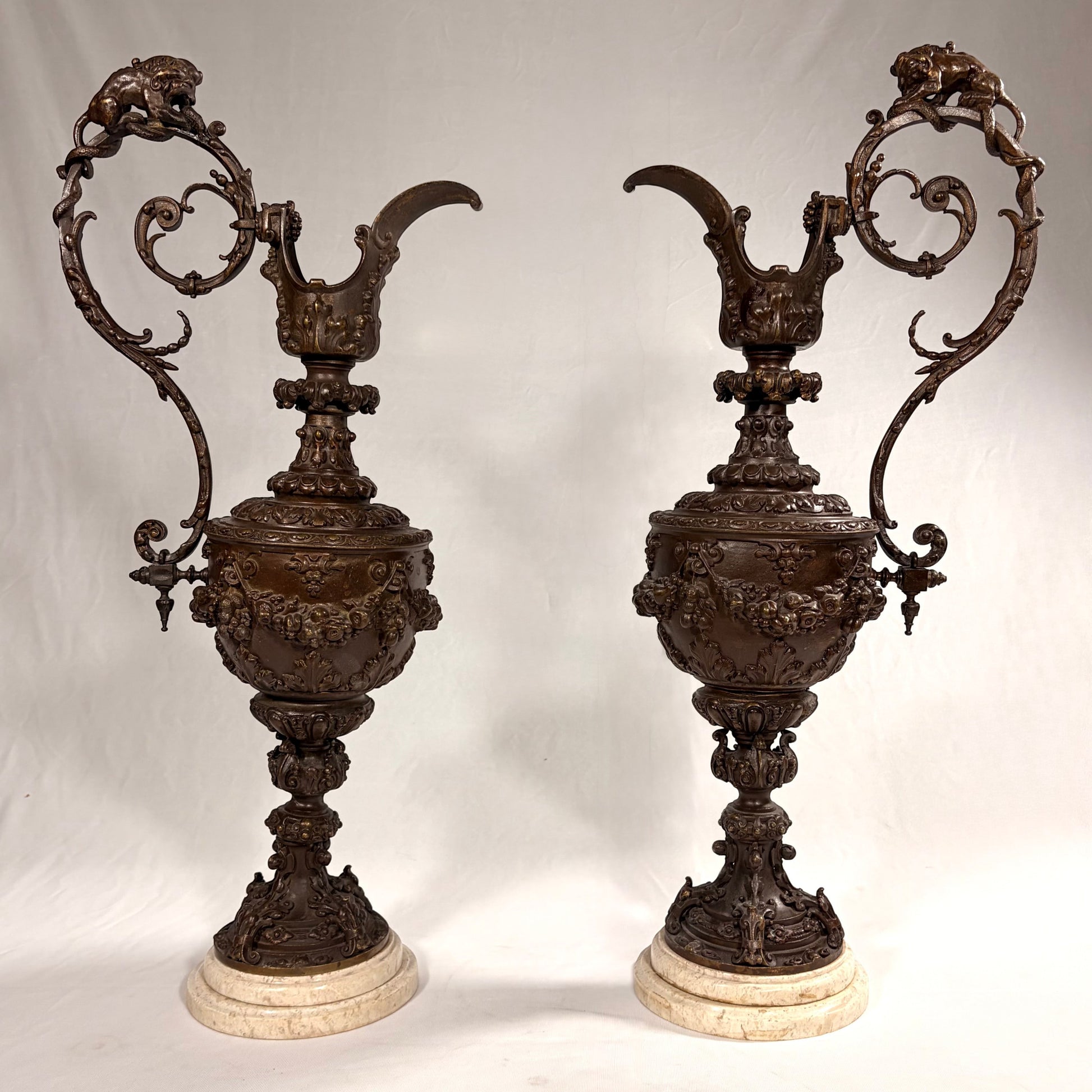 KLS Vaults pair of 19th-century Rococo Revival patinated bronze ewers with lion and serpent handles on marble bases.