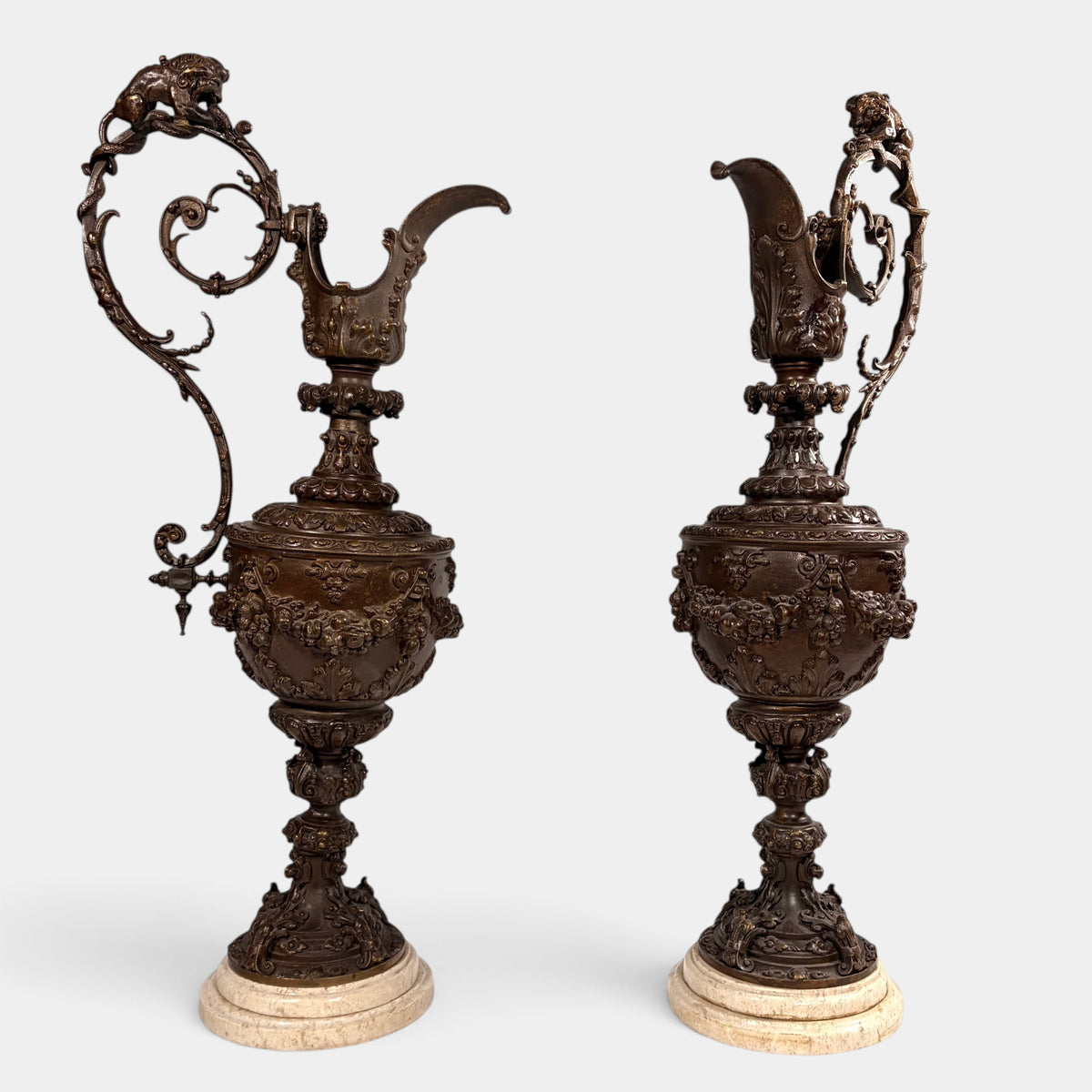 KLS Vaults pair of 19th-century Rococo Revival patinated bronze ewers with lion and serpent handles on marble bases.
