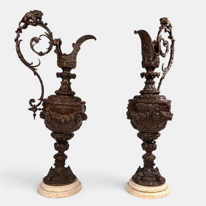 KLS Vaults pair of 19th-century Rococo Revival patinated bronze ewers with lion and serpent handles on marble bases.
