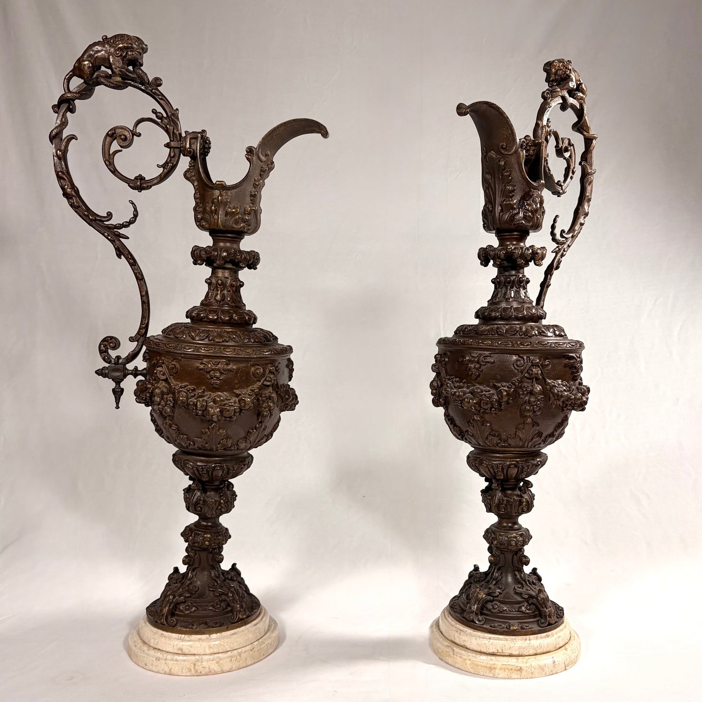 KLS Vaults pair of 19th-century Rococo Revival patinated bronze ewers with lion and serpent handles on marble bases.
