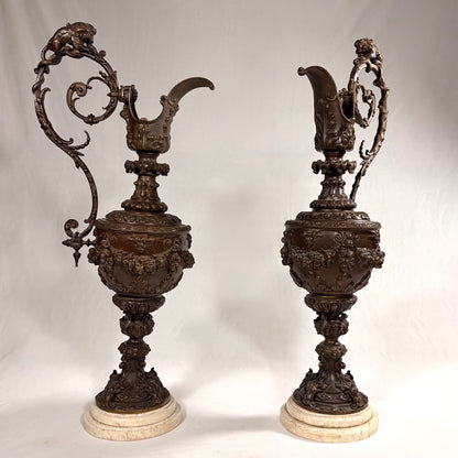 KLS Vaults pair of 19th-century Rococo Revival patinated bronze ewers with lion and serpent handles on marble bases.