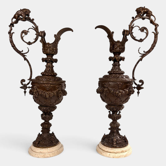 KLS Vaults pair of 19th-century Rococo Revival patinated bronze ewers with lion and serpent handles on marble bases.
