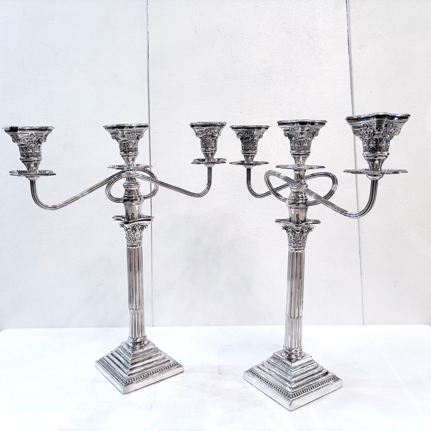 KLS Vaults pair of George III style sterling silver three-light candelabra with Corinthian columns and ornate detail.
