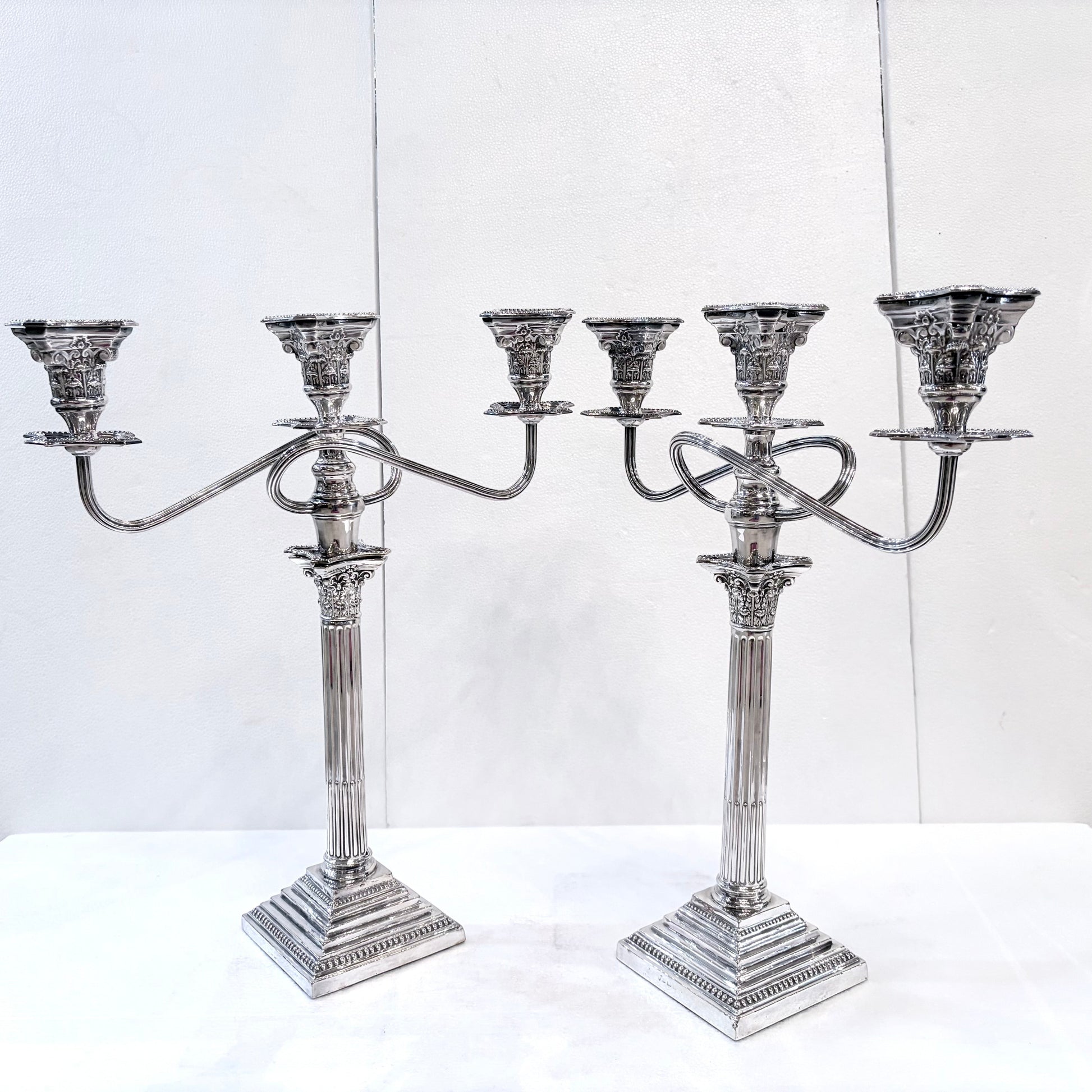 KLS Vaults pair of George III style sterling silver three-light candelabra with Corinthian columns and ornate detail.