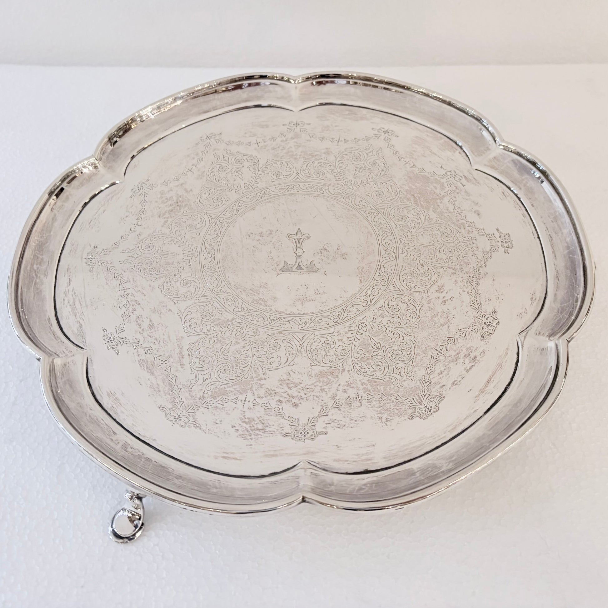 KLS Vaults 1937 sterling silver salver with Chippendale scalloped rim, foliate engraving, and central armorial crest.