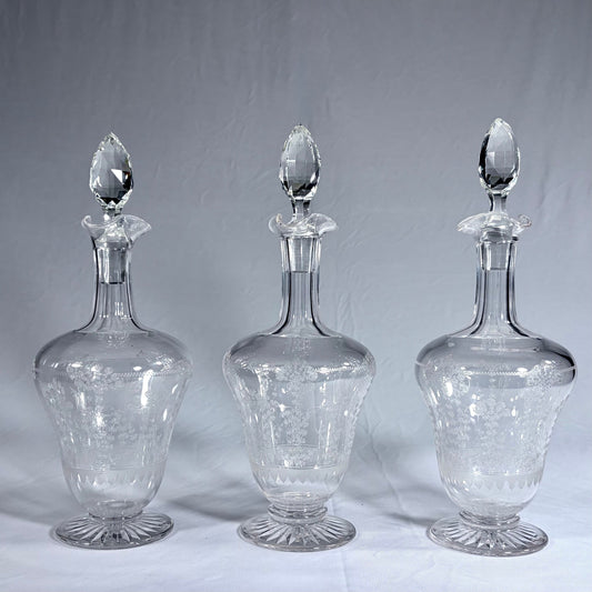 KLS Vaults set of three Stuart crystal decanters with acid-etched botanical motifs and multifaceted stoppers.
