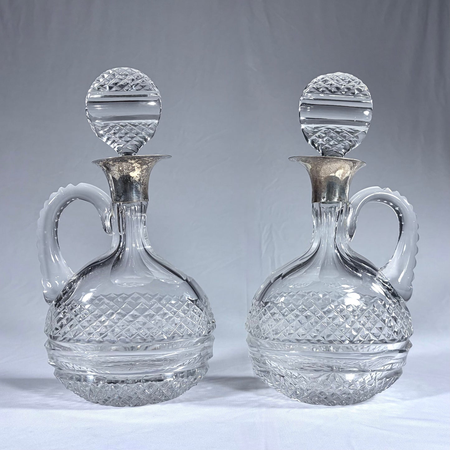 KLS Vaults pair of Victorian diamond-cut crystal claret jugs with silver collars and matching disc-form stoppers.