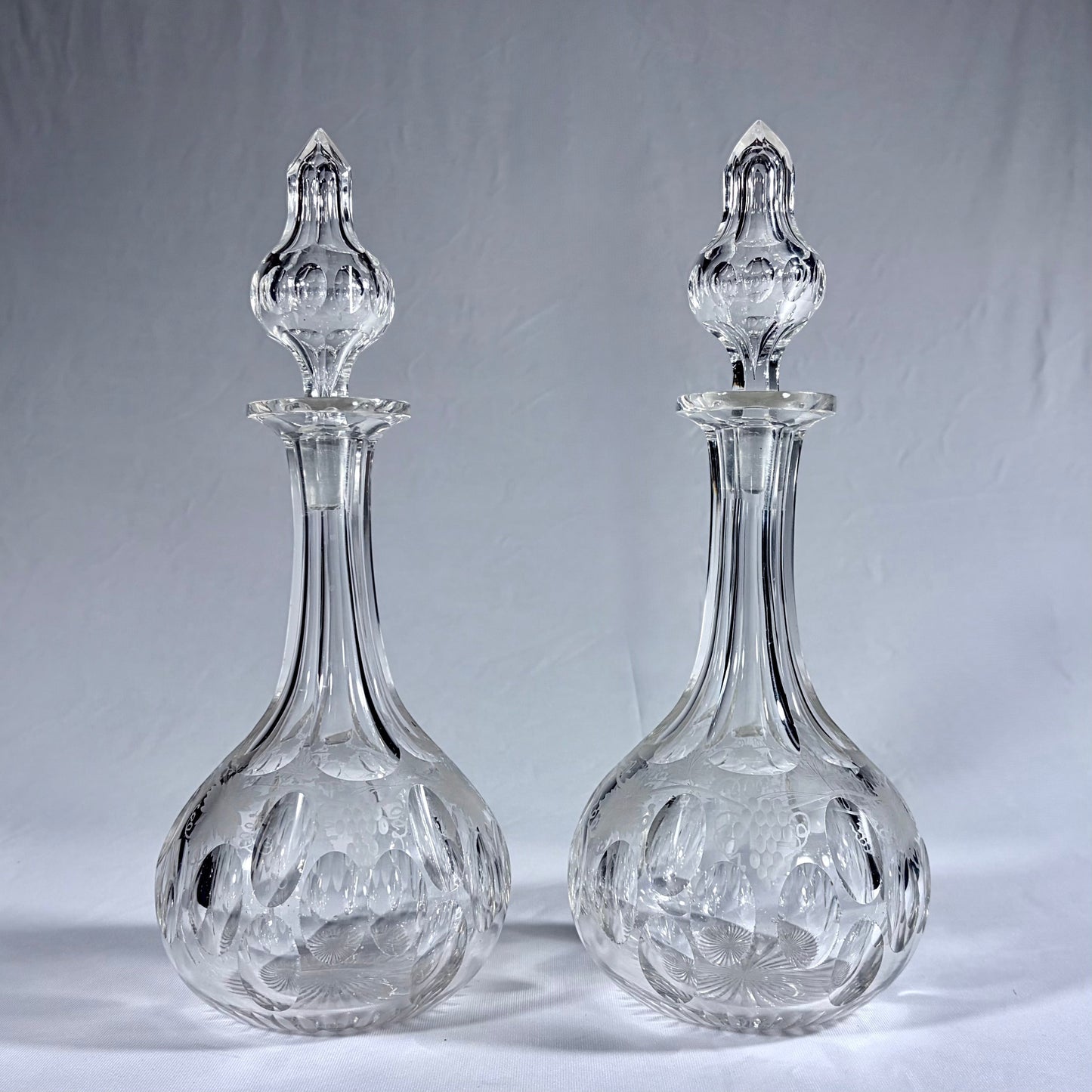 KLS Vaults pair of Victorian lead crystal decanters with grapevine engraving, oval facets, and original spired stoppers.