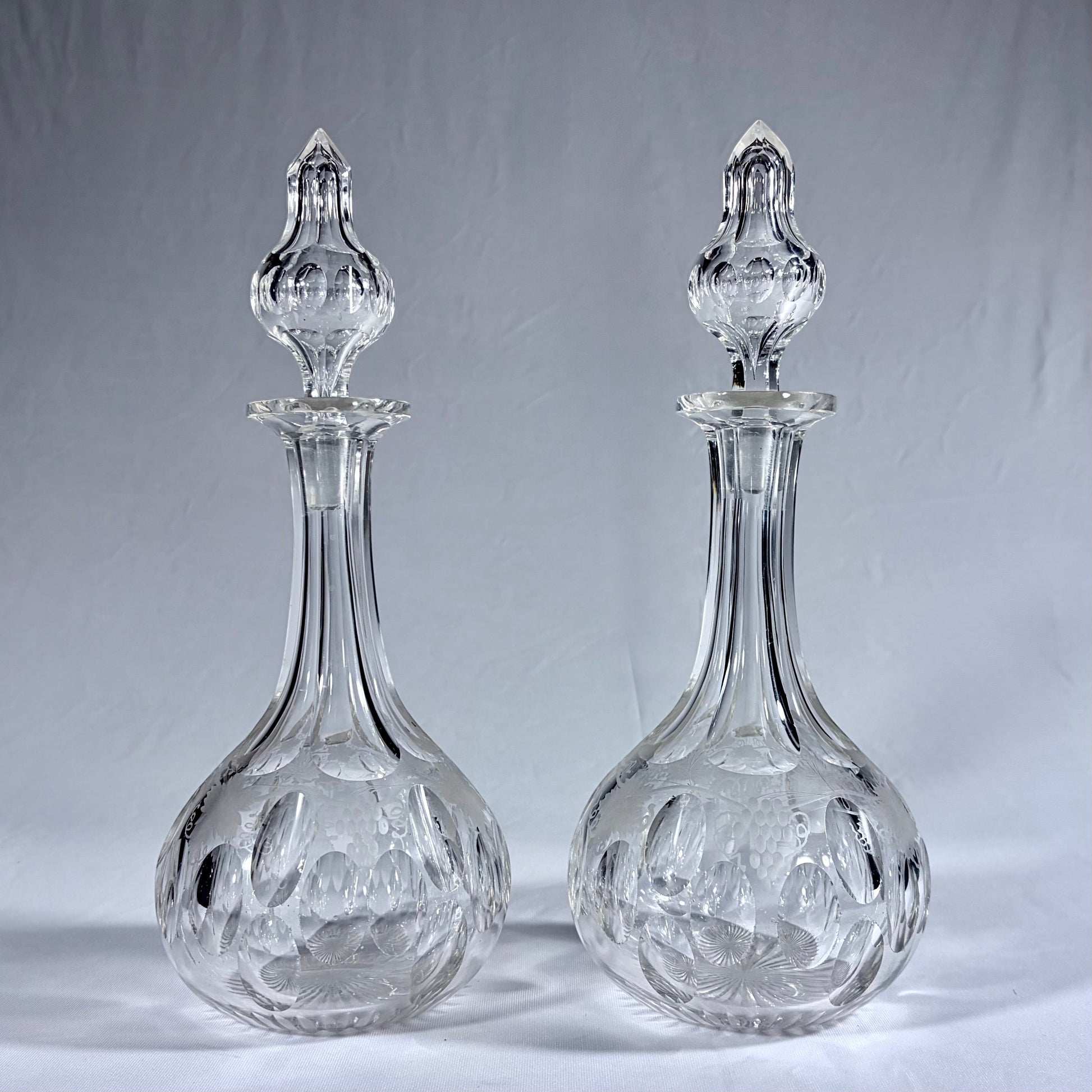KLS Vaults pair of Victorian lead crystal decanters with grapevine engraving, oval facets, and original spired stoppers.