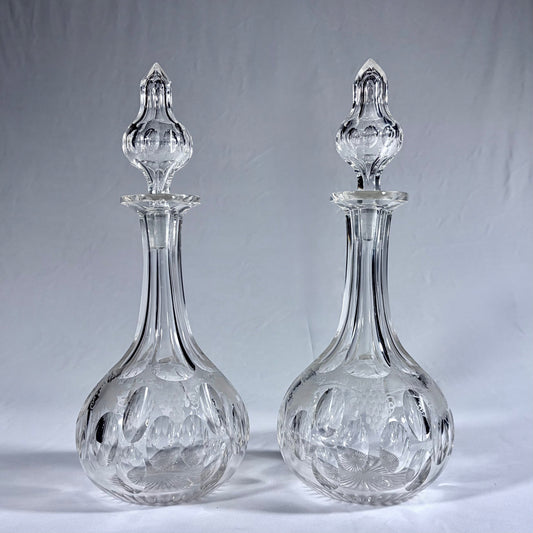 KLS Vaults pair of Victorian lead crystal decanters with grapevine engraving, oval facets, and original spired stoppers.